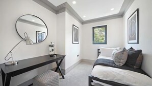 Una camera da letto con un letto, una scrivania, una sedia, uno specchio e quadri appesi al muro.