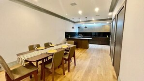 Zona pranzo moderna con tavolo in legno, sedie e una cucina sullo sfondo.