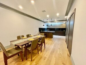 A modern dining area with a wooden table, chairs, and a kitchen in the background. - Luxury 4BR Camden Villa w/ Parking & Garden (London)