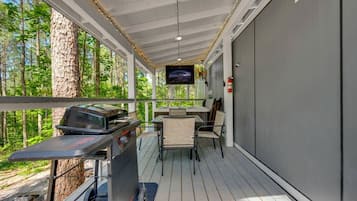 Una terraza exterior con una parrilla, asientos y una pantalla de televisión.