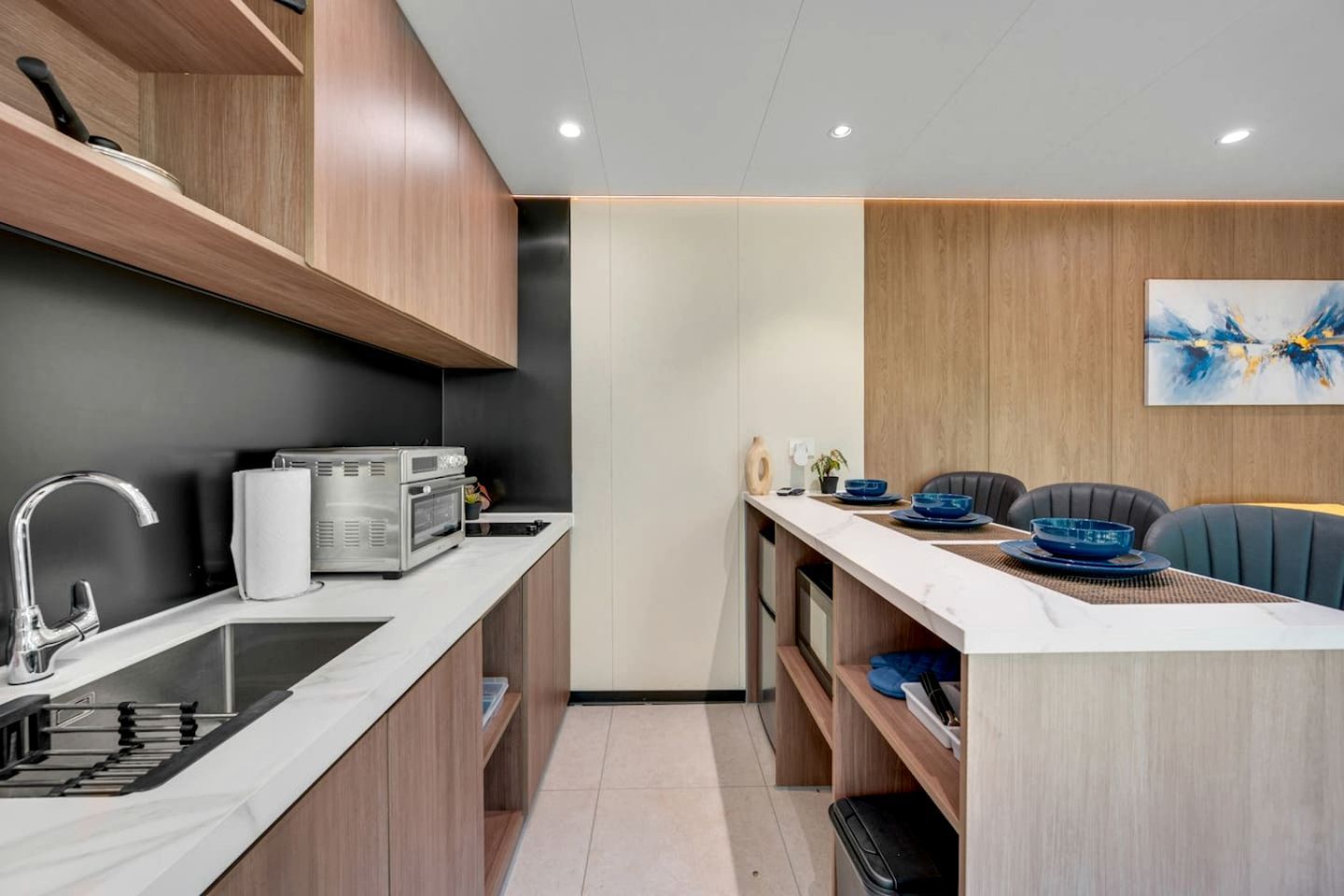 A compact kitchen with modern appliances, a dining area with a table set for two, and a minimalist decor.