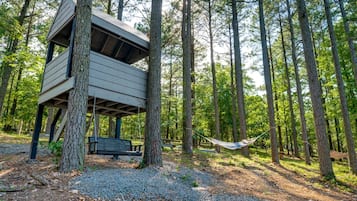 A treehouse with a bench and hammock in a forest.