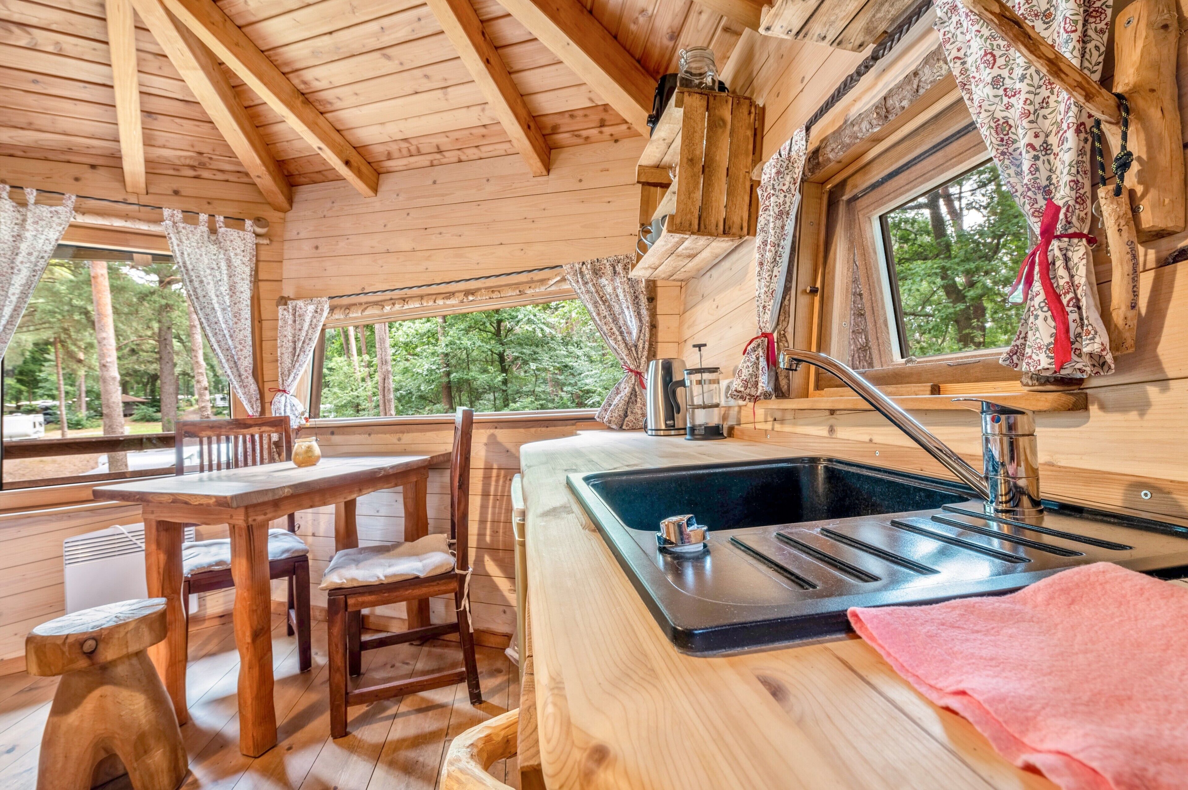 Ein Interieur einer Holzhütte mit Esstisch, Stühlen, Spüle und einem Fenster mit Vorhängen.