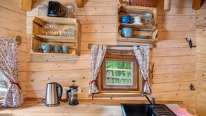 A wooden interior with a kitchen area, including a sink, a coffee maker, and shelves with glassware. - Treehouse 'Wernerwald' with Balcony and Wi-Fi (Cuxhaven)