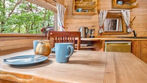 A wooden cabin interior with a dining table, chairs, a kettle, and a coffee maker. - Treehouse 'Wernerwald' with Balcony and Wi-Fi (Cuxhaven)