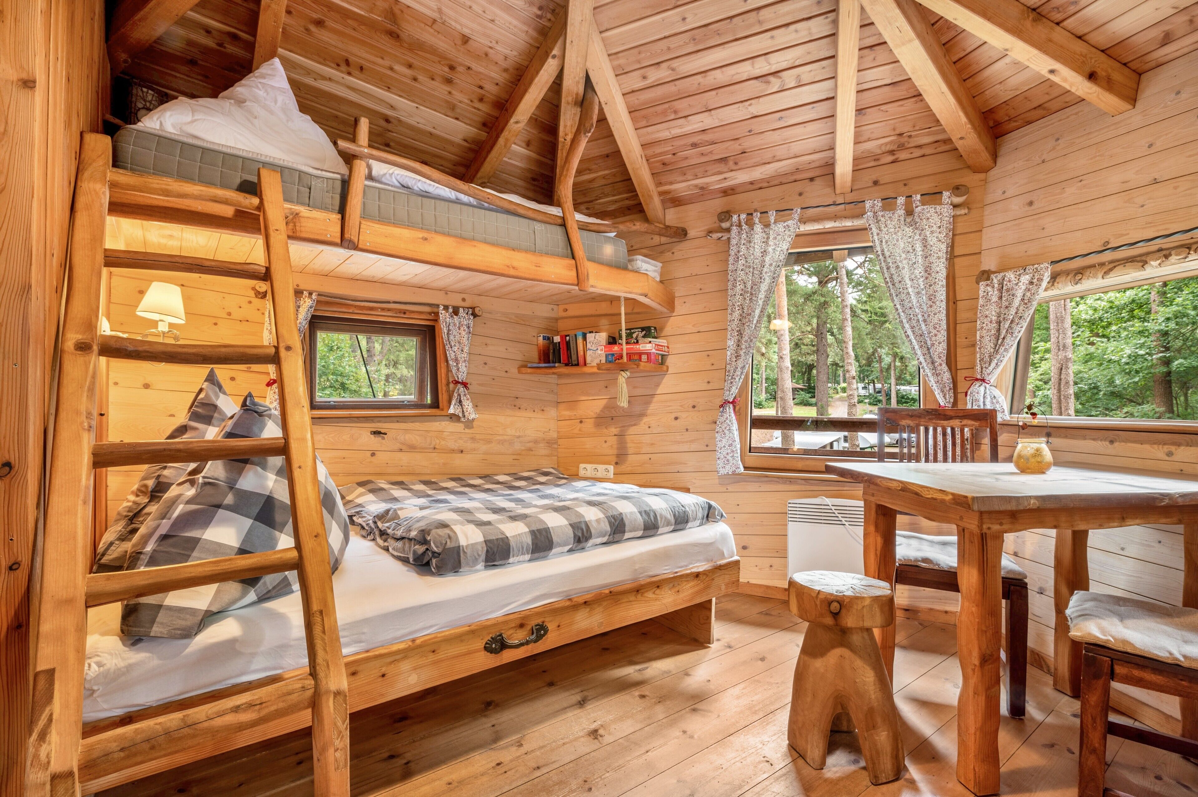 Eine Holzhütte mit Etagenbett, Schreibtisch und Fenster mit Blick auf einen Wald.