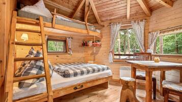 Eine Holzhütte mit Etagenbett, Schreibtisch und Fenster mit Blick auf einen Wald.