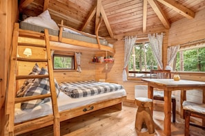 Una cabaña de madera con literas, un escritorio y una ventana con vistas a un bosque.