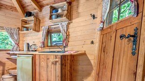 A wooden cabin interior with a kitchen area, including a sink, cabinets, and a window with curtains. - Treehouse 'Wernerwald' with Balcony and Wi-Fi (Cuxhaven)