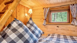 A cozy cabin room with a bed, a window with curtains, and a wall-mounted lamp. - Treehouse 'Wernerwald' with Balcony and Wi-Fi (Cuxhaven)