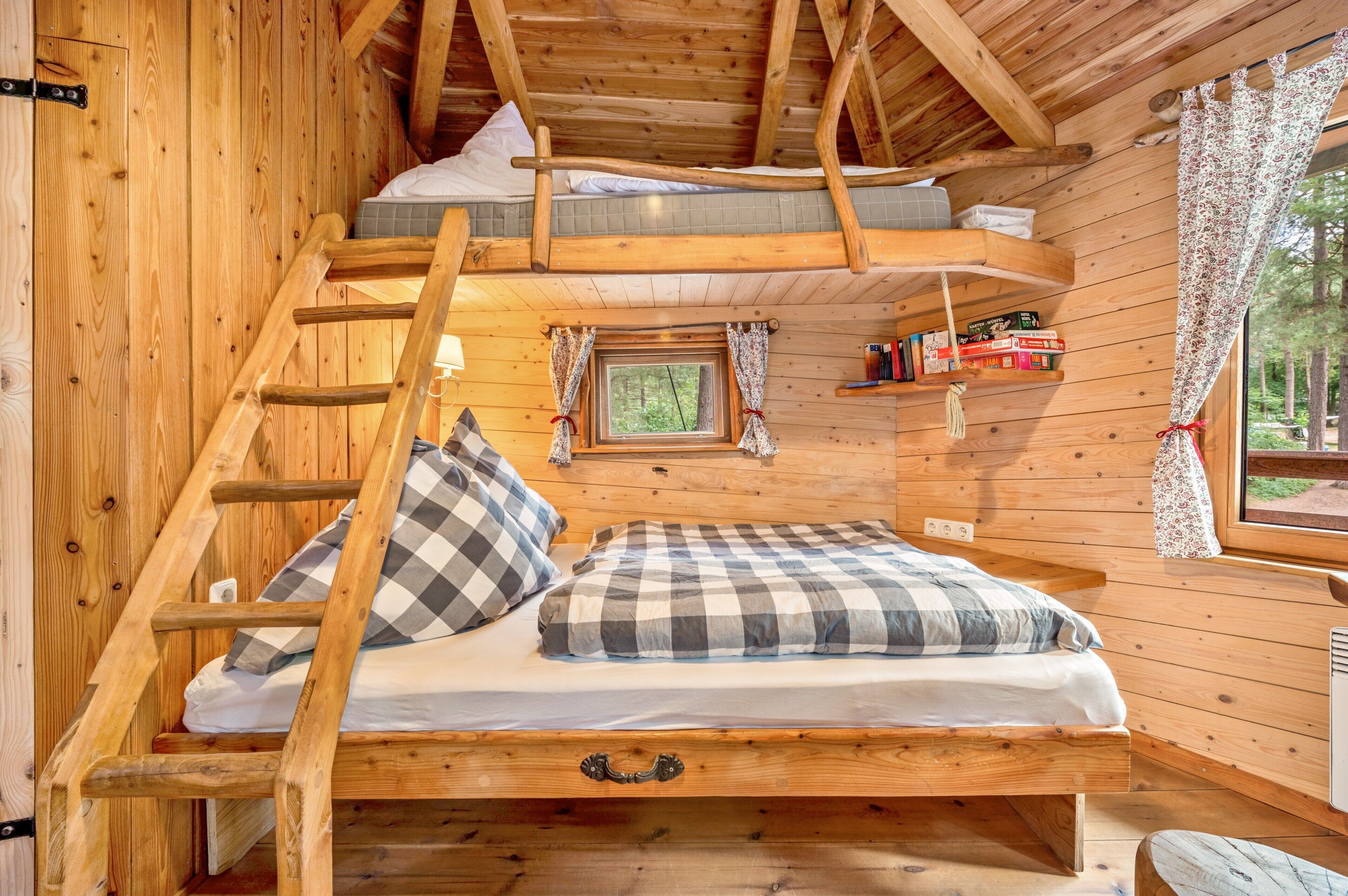 Une chambre dans une cabane en bois, avec un lit en mezzanine, une échelle, une petite fenêtre et une bibliothèque.