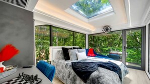A modern bedroom with a skylight, a large bed, a chessboard, and a view of greenery.