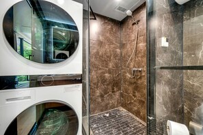 A modern bathroom with a glass-enclosed shower, a circular mirror, and a built-in washing machine.