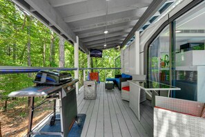A covered outdoor area with a grill, seating, and a view of the forest. - Space-Themed Luxury Pod with Hot Tub Near Broken Bow Lake, Oklahoma (Broken Bow)