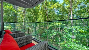 A glass-enclosed outdoor seating area with wicker furniture and a red cushion.