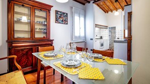 A dining area with a glass table set for four, surrounded by wooden chairs and a cabinet with glass doors. - Vellutini (Florence)