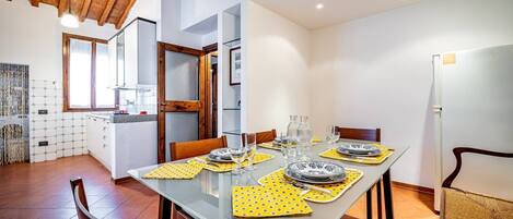 A dining area with a glass table set for four, wooden chairs, and a kitchen in the background.