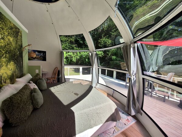 A bedroom with a large bed, a view of the outdoors, a small table, and a chair.