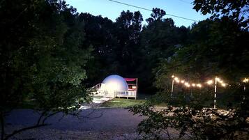 A dome-shaped building with a red roof, surrounded by trees and a gravel path.