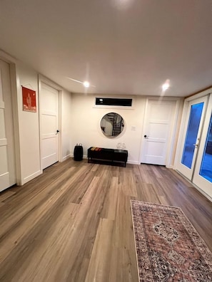 Een hal met houten vloer, een bankje, een ronde spiegel en een vloerkleed.