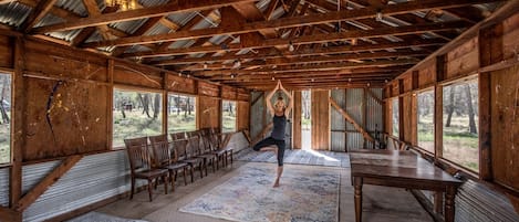 Una habitación rústica de madera con techo alto, ventanas amplias y una colchoneta de yoga en el suelo.