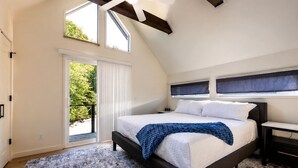 Ein Schlafzimmer mit Bett, Nachttisch, einem Fenster mit Jalousien und Blick ins Grüne.