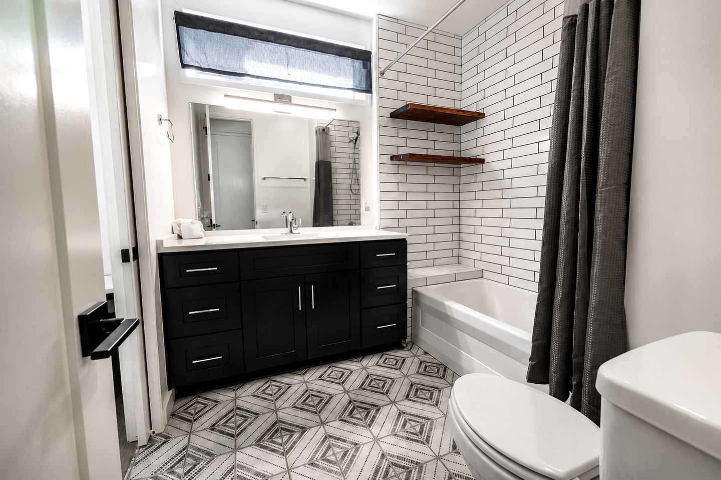 A modern bathroom with a white bathtub, black cabinets, and a patterned floor.