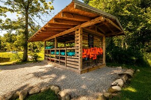 Eine Holzhütte mit Kiesweg, umgeben von Bäumen und einem Gewässer.