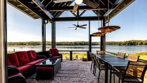 Ein überdachter Außenbereich zum Sitzen mit Blick auf einen See, inklusive Deckenventilator und Tisch mit Stühlen.