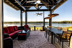 Ein überdachter Außenbereich zum Sitzen mit Blick auf einen See, inklusive Deckenventilator und Tisch mit Stühlen.