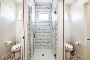 A narrow bathroom with white tiled walls and floor, a shower area, and two toilets. - Modern Waterfront Home With Lake Views in Water’s Edge Tennessee (Tracy City)
