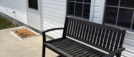 A bench outside a building with a window and a door.