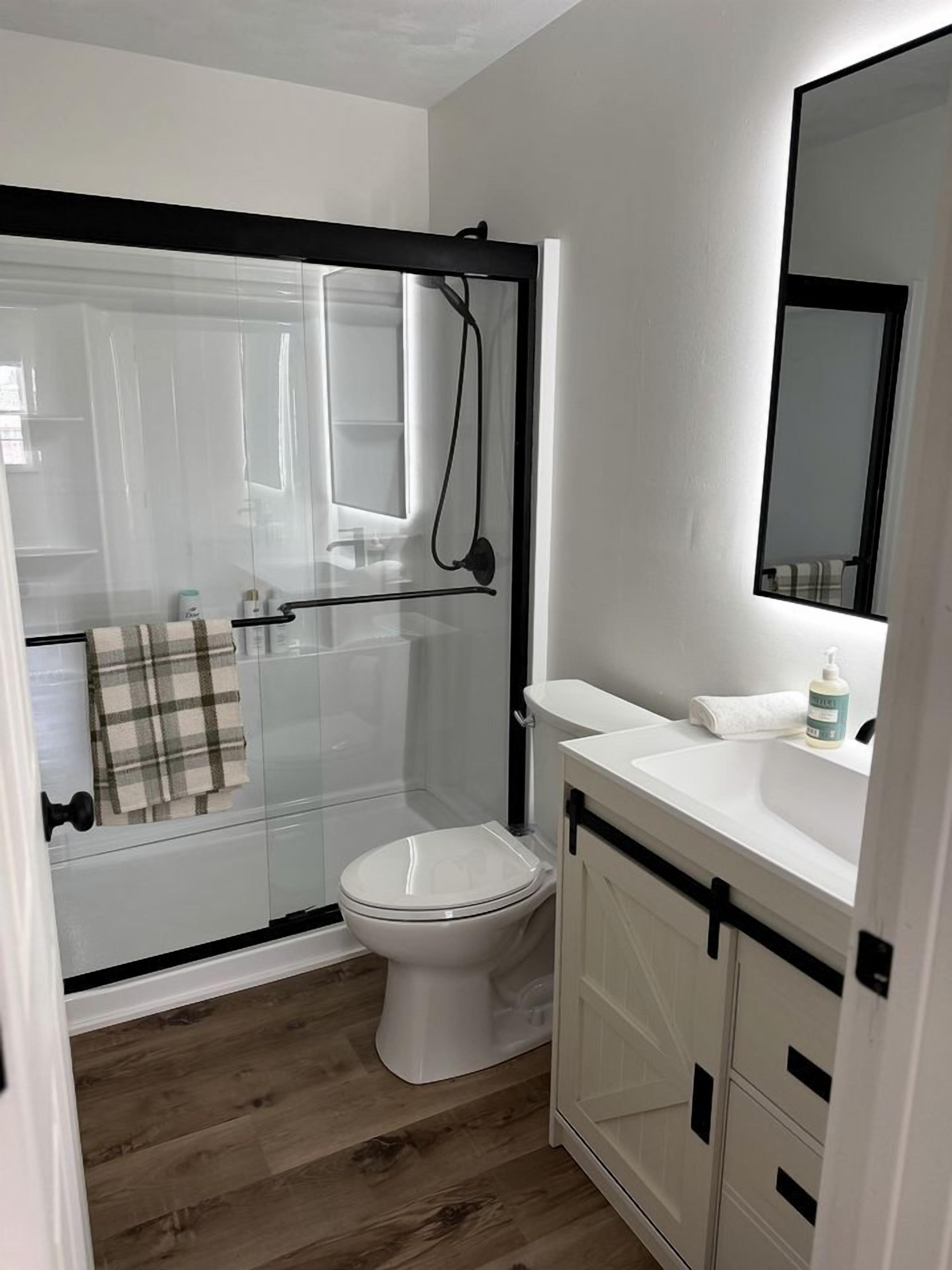 A bathroom with a glass shower enclosure, a white toilet, a sink with a mirror, and a towel rack.