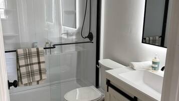 A bathroom with a glass shower enclosure, a white toilet, a sink with a mirror, and a towel rack.