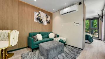 Una sala de estar moderna con un sofá verde, un sillón blanco con capitoné, un reposapiés gris y arte abstracto en la pared.