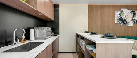A compact kitchen with a sink, microwave, and oven, wooden cabinets, and a small dining area with a couch.