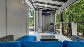 A covered outdoor area with a sofa, a grill, and a television.