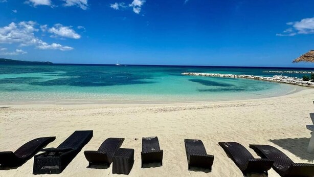 Una spiaggia con acque cristalline turchesi, una riva sabbiosa e sedie a sdraio.