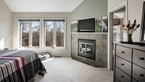 Ein Schlafzimmer mit einem Bett, einem Kamin, einem Fernseher und großen Fenstern.
