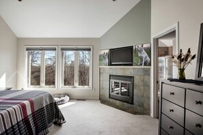 A bedroom with a bed, a fireplace, a TV, and large windows. - Exquisite Mountain Cabin Retreat near Cacapon River in West Virginia (Hedgesville)