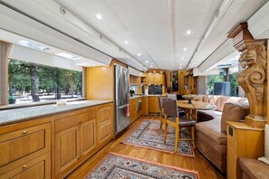 Cocina espaciosa en una casa rodante, con armarios de madera, un refrigerador y un comedor con sofá y sillas.