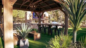 An outdoor patio with a wooden pergola, green chairs, and a dining table.