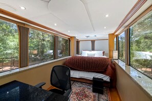 Un dormitorio con una cama, un escritorio y una silla. Cuenta con ventanas grandes en una pared.