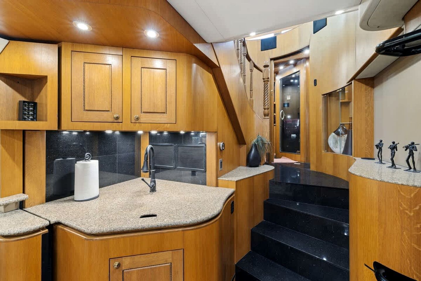 A compact kitchen with wooden cabinetry, a granite countertop, and a stainless steel sink.