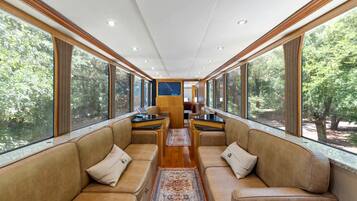 L'intérieur d'un wagon de train, avec des sièges en cuir, de grandes fenêtres et une table centrale.