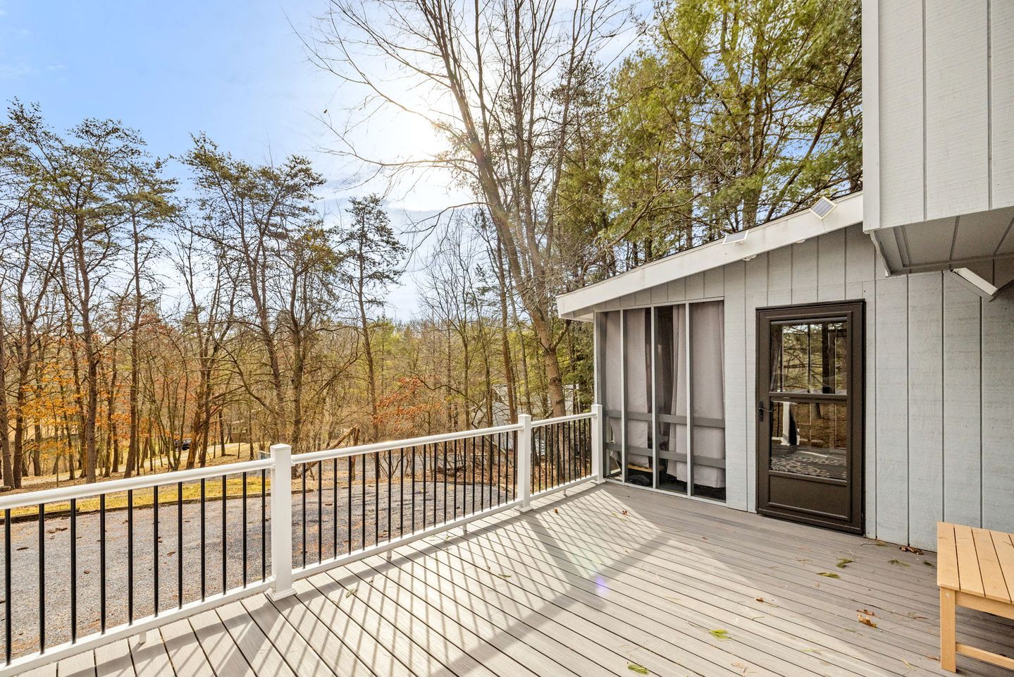 A wooden deck with a white railing, a door with a window, and a bench.