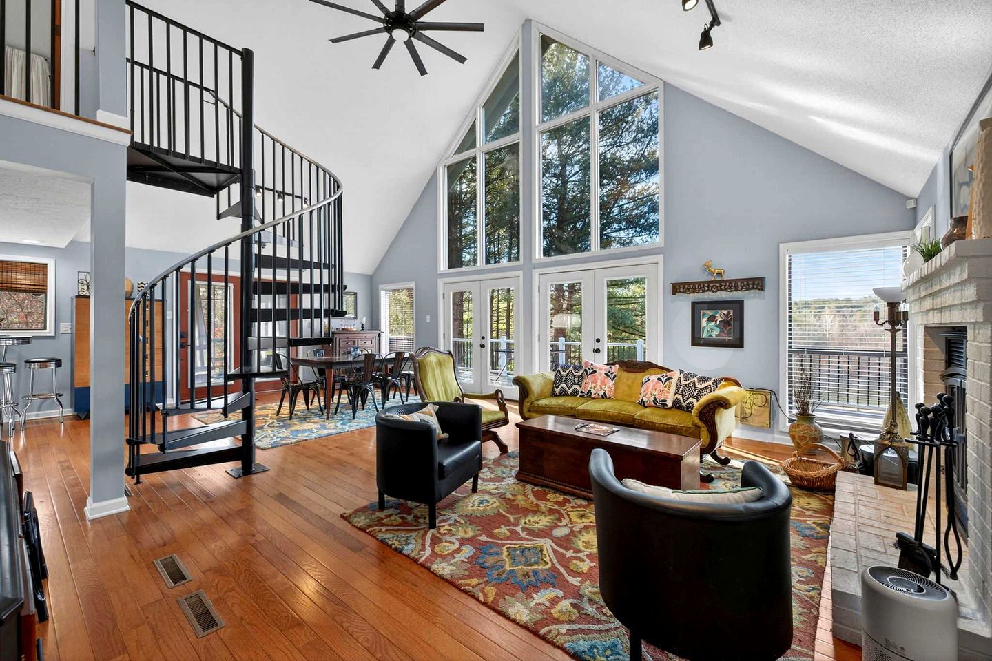 A spacious loft with a high ceiling, a spiral staircase, a large dining area, and a cozy seating area with a fireplace.