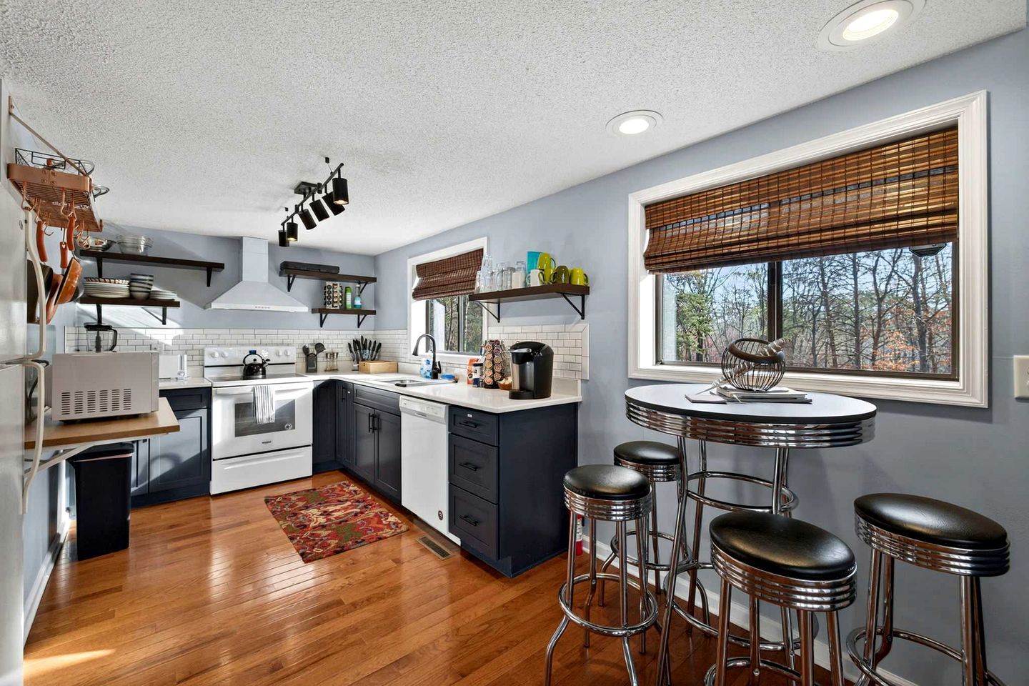 A modern kitchen with a central island, bar stools, and a window with blinds.