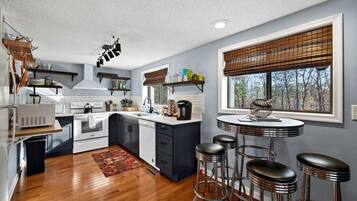 A modern kitchen with a central island, bar stools, and a window with blinds.
