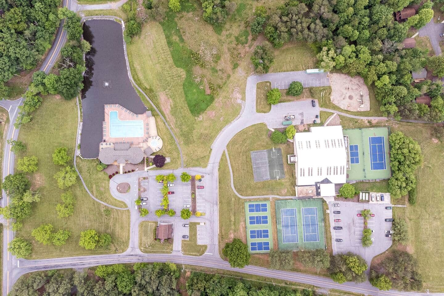 An aerial view of a property with a swimming pool, tennis courts, and a parking lot.